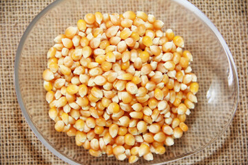 Small yellow dry grains of natural corn in a decorative plate on a brown background