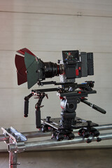 side view of a professional movie camera that stands on a camera trolley with wheels and rails. visible lens, monitor, smooth control knobs