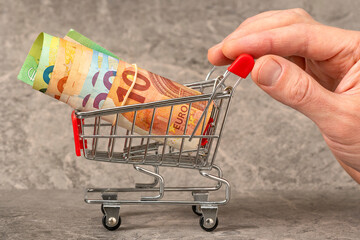 Hand pushing a small shopping cart with money roll