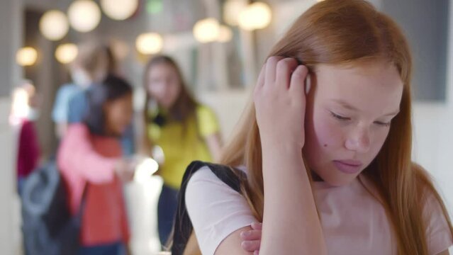 Students laughing and pointing to lonely sad girl standing aside. Realtime