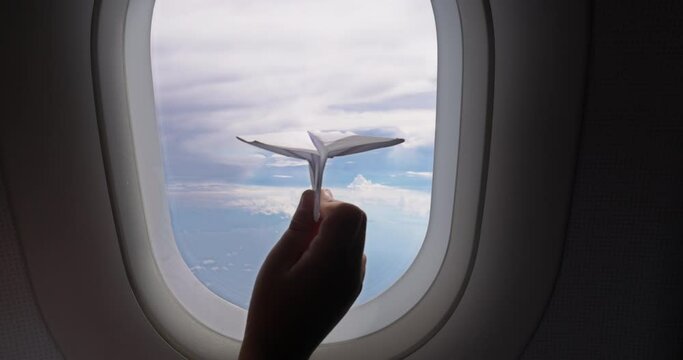 Kid plays with paper plane on board plane near window. An ambitious girl from childhood sets herself goal of becoming pilot. Girl already at an early age decided on the future profession of a pilot.
