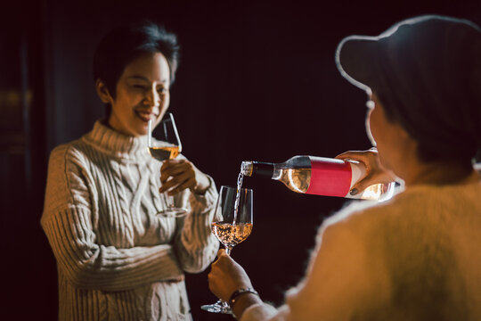 Couple of woman in sweaters pouring wine into glasses enjoy free time.