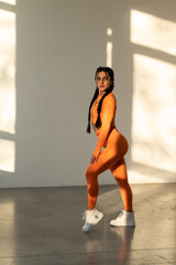 Beautiful young woman with natural make-up, dressed in a orange sports uniform, posing in the studio on a white wall.Advertising sportswear and yoga wear. Healthy lifestyle, sport