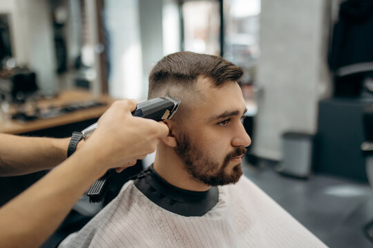 A close-up photo of a man's hair cut. A professional hairdresser cuts a man with beard in a barbershop. Men's beauty salon.