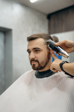 A close-up photo of the men's haircut process. A professional hairdresser cuts a man's hair with a clipper in a barbershop. Men's beauty salon.