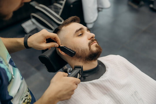 A close-up photo of a man's beard haircut. A barber cuts a beard in a barbershop. Beard trimming in a beauty salon for men