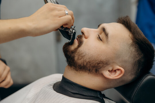 A close-up photo of a man's beard haircut. A barber cuts a beard in a barbershop. Beard trimming in a beauty salon for men