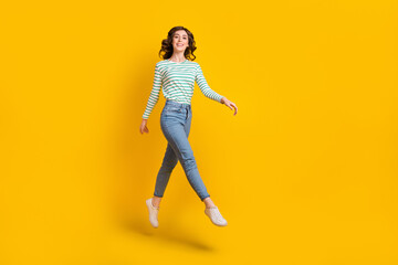 Fototapeta na wymiar Full length photo of pleasant optimistic cute girl wear striped shirt denim pants flying dancing isolated on yellow color background