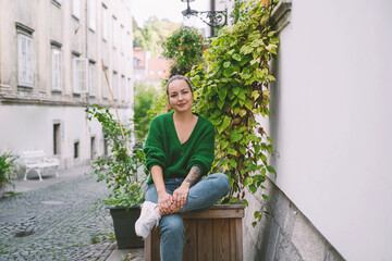Photo of friendly smiling attractive woman on background of green hedge in the street of european...