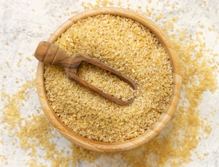 Raw Dry bulgur wheat grain in a wooden bowl with a scoop top view. Mediterranean cuisine