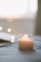 Cozy still life composition with a scented burning candle in glass jar in bed close up. Good morning. Cozy home