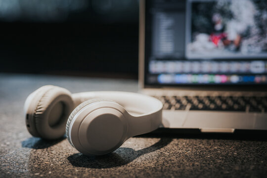 White Headphones And Laptop On Table In Dark Room.