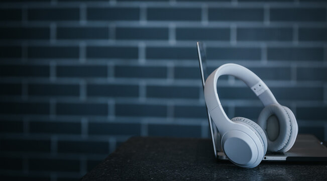 White Headphones And Laptop On Table In Dark Room.