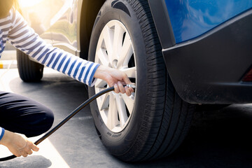 Woman inflates the tire. Woman checking tire pressure and pumping air into the tire of car wheel. Car maintenance service for safety before travel. Tire inflating point. Filling air in the tyre of car - obrazy, fototapety, plakaty