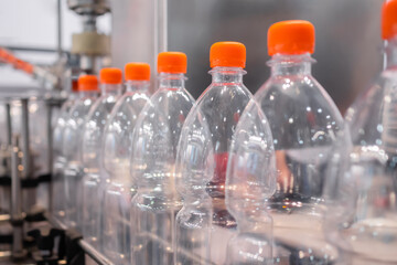 Row of empty pet lemonade bottles with orange caps on conveyor belt of automatic liquid filling machine at plastic exhibition - close up. Manufacturing, industry and technology equipment concept