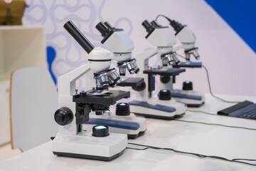 Microscopes on white table at medical technology exhibition, trade show. Laboratory equipment, science, medical, optical, pharmaceutical and education concept