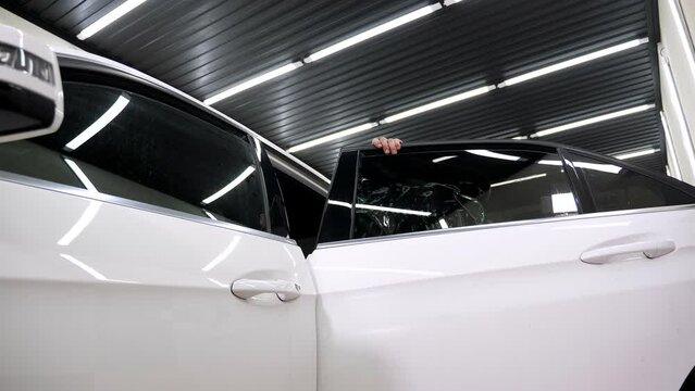 Close-up installation of tinting film on the windows of a new white car, removal of excess water from under the film with a spatula.