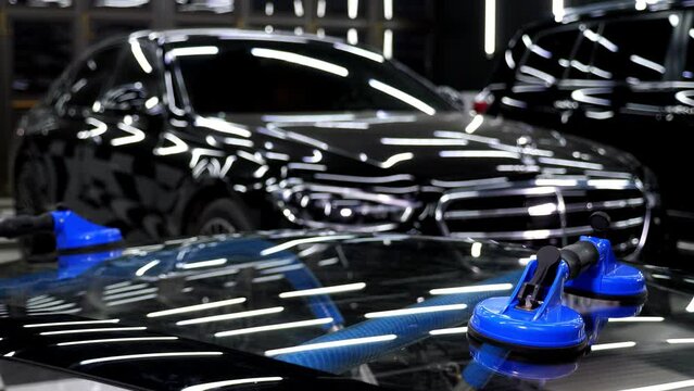 The glass of the car is a close-up in the room, taken with the help of professional suction cups. Bright illuminated car service with a car. The process of car repair.