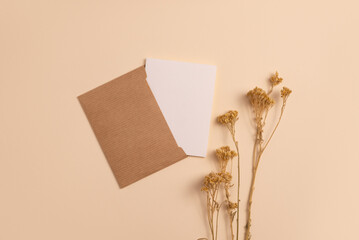 Mockup of an open invitation card made of ecological craft paper and decorated with a composition of dry flowers placed vertically on a beige background