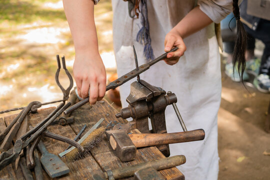 Professional blacksmith woman in historical costume working with metal on anvil at outdoor workshop - close up view. Handmade, reenactment, craftsmanship, medival concept