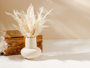 Vase with pampas grass on the table with wooden box organizer and copy space, warm shadows. Aesthetic interior, scandinavian home  decoration with natural eco friendly grass - obrazy, fototapety, plakaty