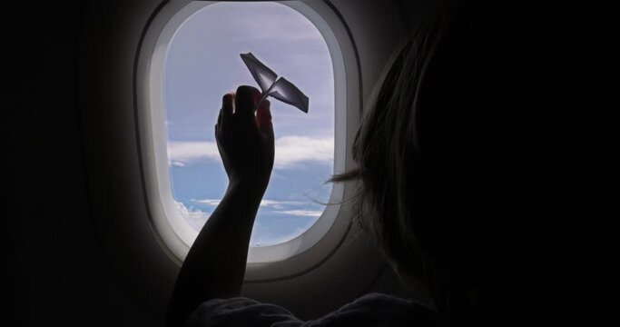 A boy in love with sky plays with paper plane, imagining how he will one day pilot real one on his own. A child in flight on an airplane plays with paper toy by the window and looks lovingly at sky.