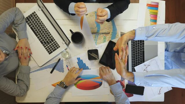 Young tired managers stretches hands sitting at table in office. Professional coworkers ready to continue working with documents at boardroom. Top view to male and female arms of entrepreneurs