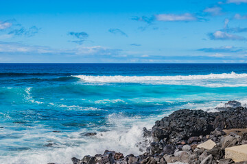 Black and volcanic rocks wetted by sea waves in blue gradient at Santa Bárbara beach, São Miguel...