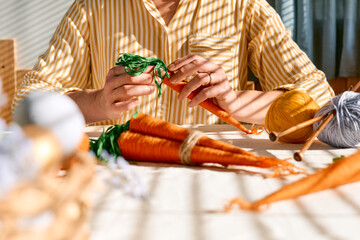 Woman making craft wool thread carrots for Easter decoration. Minimalist decor for Easter. DIY handmade craft project.
