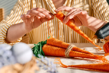 Woman making craft wool thread carrots for Easter decoration. Minimalist decor for Easter. DIY handmade craft project.