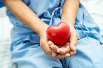 Asian elderly woman patient holding red heart in her hand on bed in hospital, healthy strong medical concept.