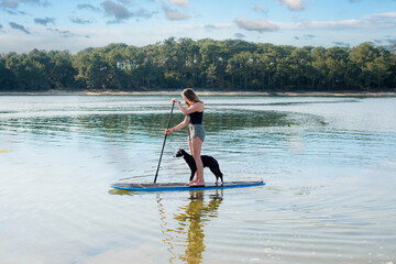 Beautiful young woman stand up paddling with her Border Collie puppy