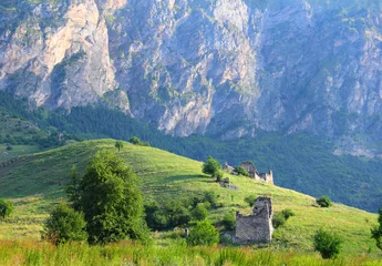Selbstklebende Fototapeten Beautiful mountain view - ruins of the ancient ingush ancestral complex Barkinhoy, green hill and barren rock at the background. Morning near Leimi village, Ingushetia, North Caucasus, Russia © little_mouse