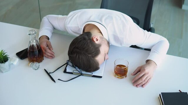 Alcoholism, drinking concept. Drunk employee sleeping at working place, holding glass with alcohol