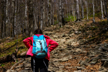 girl in pink jacket walks up a steep mountain during spring; walk in the mountains with vegetation coming to life, colourful spring in the mountains, luscious green plants