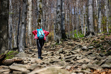 Obraz premium girl in pink jacket walks up a steep mountain during spring; walk in the mountains with vegetation coming to life, colourful spring in the mountains, luscious green plants