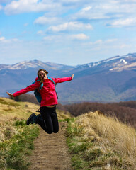 Beautiful fit happy girl in pink jacket enjoys hike in stunning colorful mountain scenery. Spring in the Bieszczady Mountains, Poland, Europe