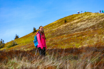 Naklejka na ściany i meble cute hiker girl with pigtails standing on the mountainous glade during spring; colorful spring in the european mountains, 