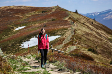 Naklejka na ściany i meble girl in pink jacket walks along a mountain ridge during spring; mountain walk with vegetation coming to life, colourful spring in the mountains