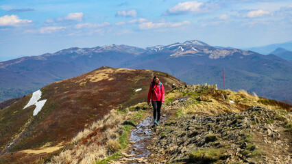 Naklejka premium girl in pink jacket walks along a mountain ridge during spring; mountain walk with vegetation coming to life, colourful spring in the mountains
