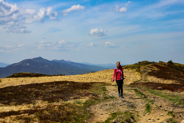 Fototapeta premium Beautiful fit happy girl in pink jacket enjoys hike in stunning colorful mountain scenery. Spring in the Bieszczady Mountains, Poland, Europe