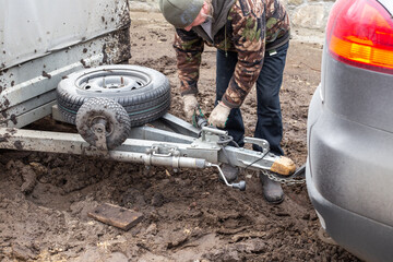 A man checking the hitch mechanism on a car trailer in bad weather