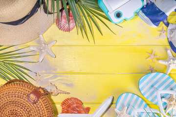 Bright sunny lighted summer vacation background, vacation and travel, beach accessories, swim suit, hat, flip flops, photo camera, sea star and shells on high-colored yellow wooden background top view