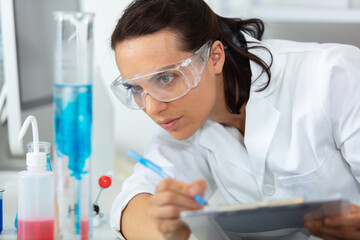 portrait of confident female scientist taking notes in chemical laboratory