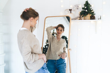 Positive young woman standing near mirror