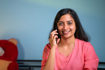 Happy young girl talking on mobile phone call while sleeping on bed at night - concept of carefree...