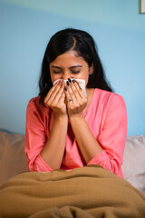 vertical shot of Young girl suffering from cold by sneezing at home whille sleeping on bed -...