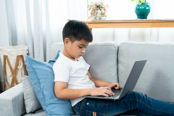 Asian boy sitting open notebook, studying online morning, sitting on living room sofa house, looks determined to study, When class was finished, they sat down to do homework that teacher ordered.