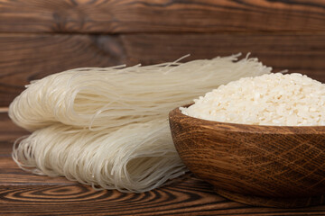 Funchoza.Dried raw rice noodles and rice on a brown wooden background.Noodles with rice flour. Diet food. Healthy food. Place for text. Place for copying.