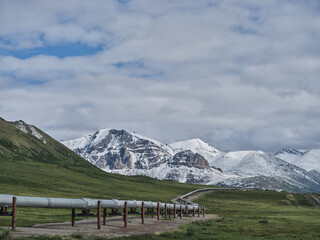 Fresh July snowfall on the mountains of the Brooks Range with the Alaska Oil Pipeline in the foreground traversing miles of empty Tundra